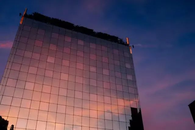 A modern skyscraper with glass facade reflecting a vibrant sunset sky.